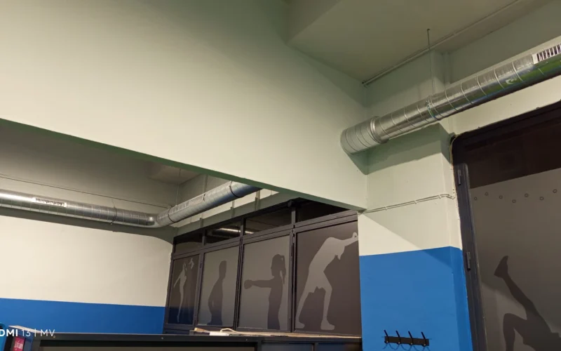 Conductos circulares de ventilación mecánica con rejillas de impulsión instalados en el techo de un recinto deportivo