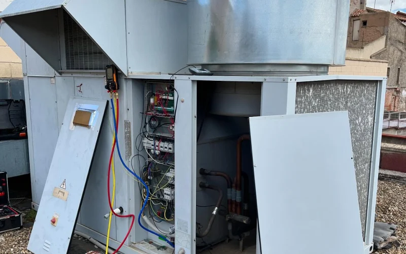 Unidad de climatización en cubierta con paneles abiertos y analizador de refrigerante conectado durante una intervención de mantenimiento